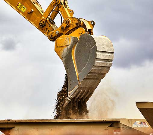 Excavator dumping a load of dirt into a dump truck.
